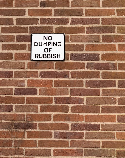 A large collection of mixed waste and rubbish bags, including black, green, and red trash bags, as well as flattened cardboard boxes, paper, and plastic packaging, piled up on a paved sidewalk curb. T